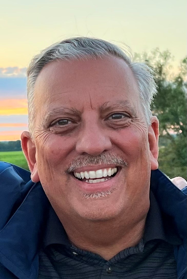 Mike Pate smiling outdoors at sunset, wearing a navy jacket