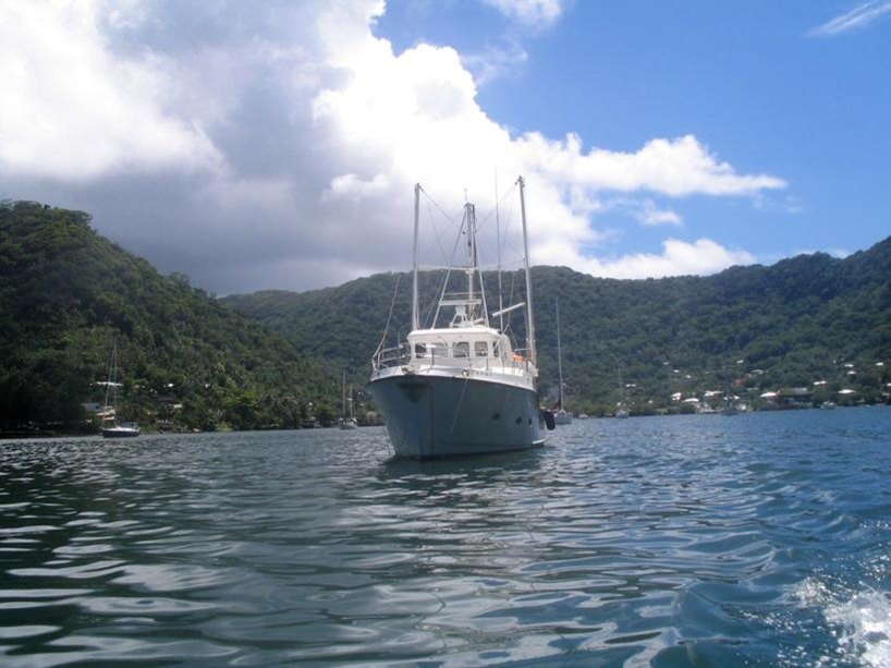 Larry Ricks' 40-foot Nordhavn at anchor in Pago Pago harbor, green mountains and white clouds behind it.